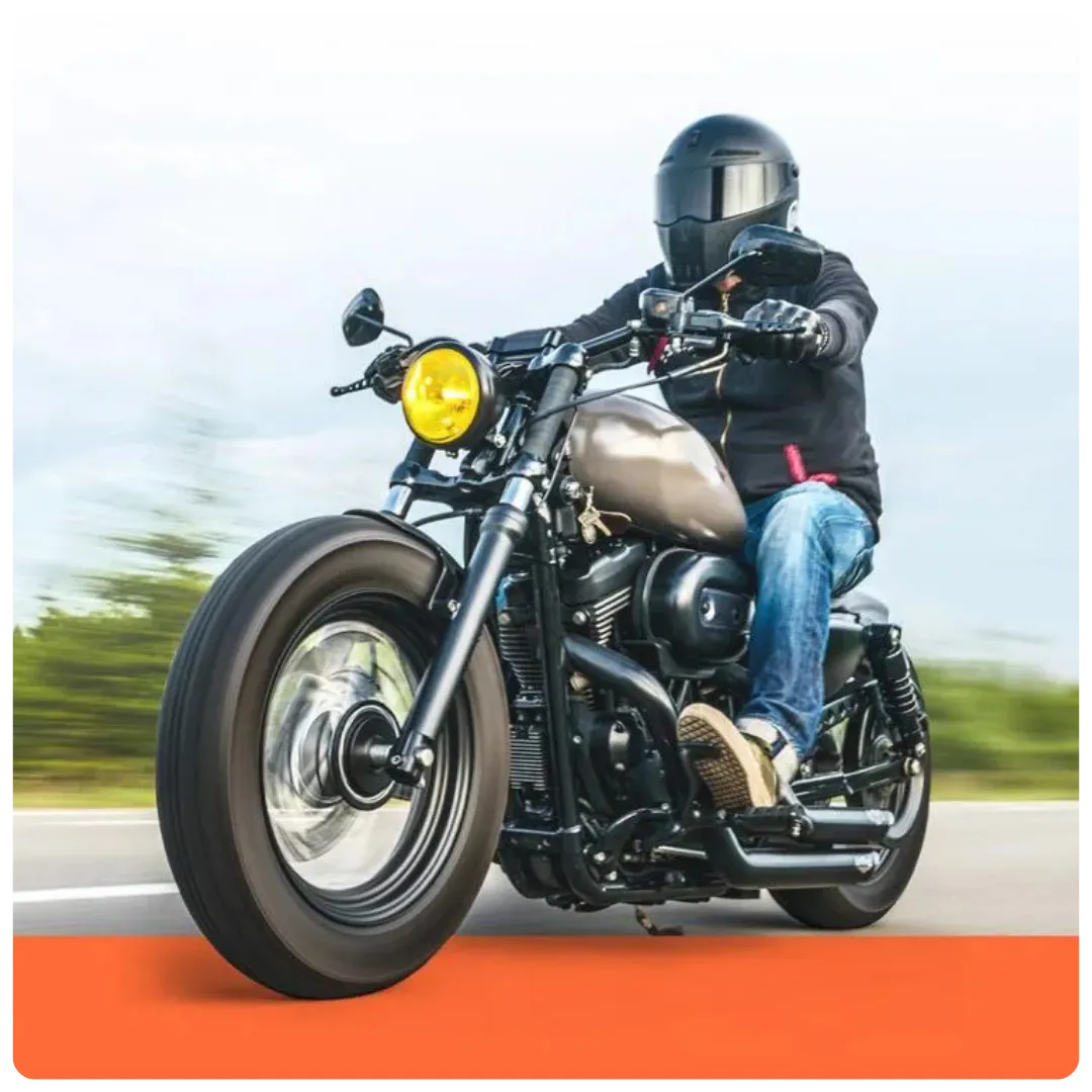 A motorcyclist in a black helmet and jacket riding a custom bobber-style motorcycle with a matte tank and yellow headlight on an open road.